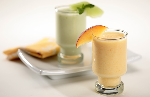 Green and orange smoothies in glasses on a table with plates.